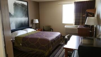 A hotel room with a bed, a desk, a chair, a lamp, a window with curtains, an air conditioner, and a painting on the wall.