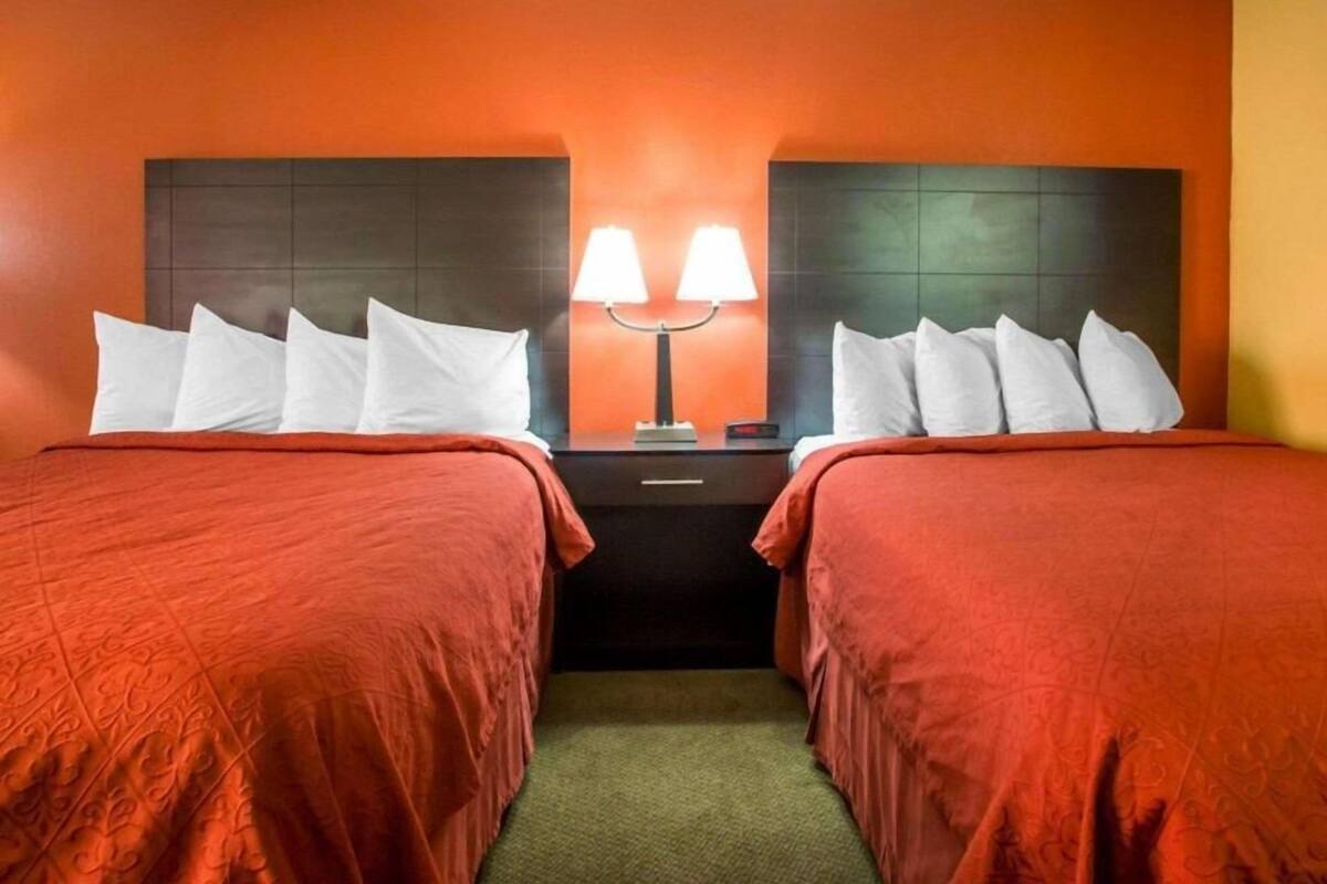 A hotel room with two beds, a nightstand with lamps, and a wall with a textured pattern.