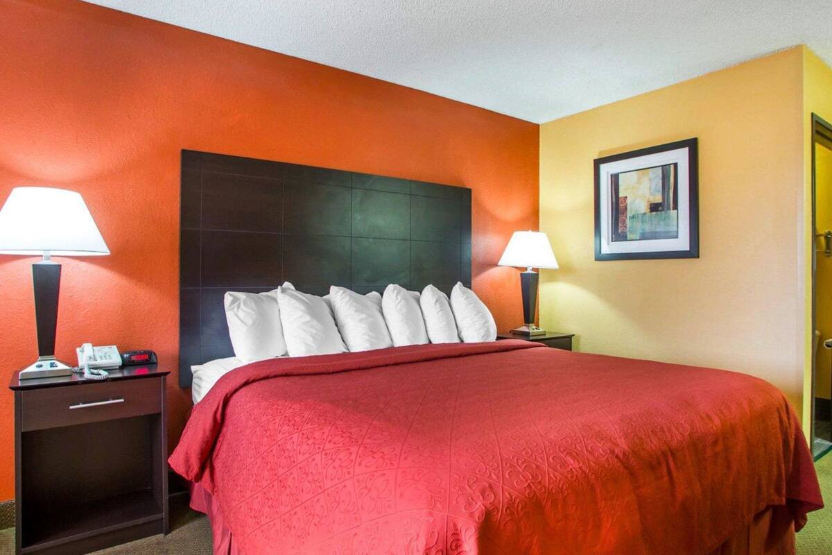 A hotel room with a large bed, two bedside tables with lamps, a framed picture on the wall, and a door to the right.