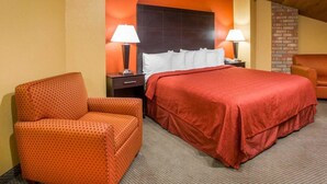 Habitación de hotel con cama, dos mesitas de noche, dos lámparas, un sillón estampado de lunares y una pared decorativa de ladrillo.