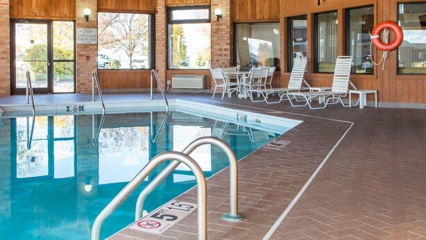 Una piscina interior con agua cristalina, rodeada de sillones de descanso y una pared de ladrillo.