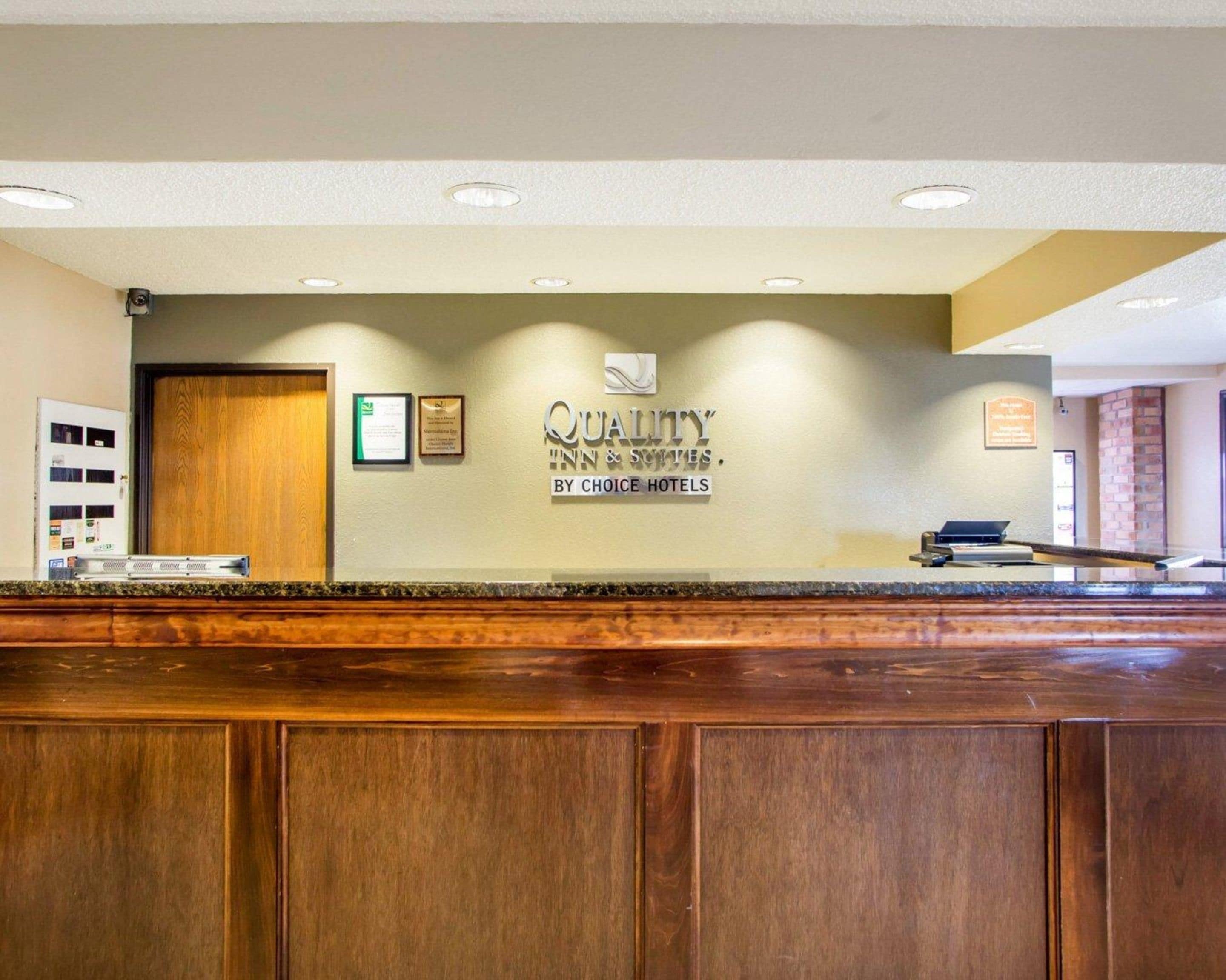 A reception desk with a sign reading "Quality Inn & Suites by Choice Hotels" and a wooden door to the left.