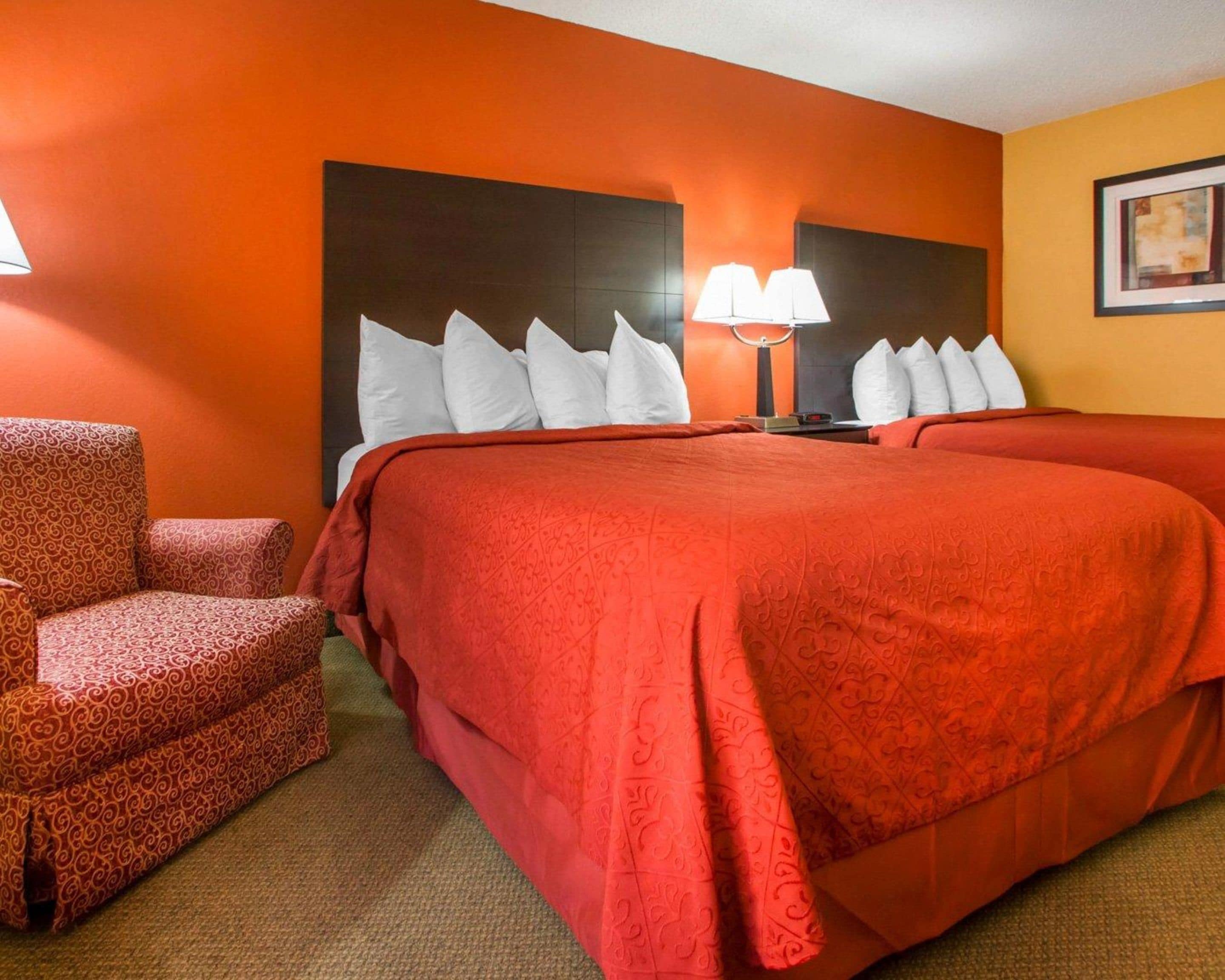 Habitación de hotel con una cama grande, dos lámparas de noche, un cabecero y un sillón estampado.