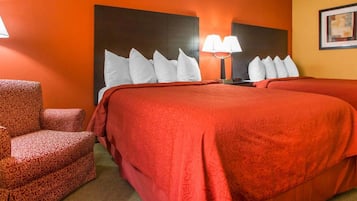 Habitación de hotel con una cama grande, dos lámparas de noche, un cabecero y un sillón estampado.