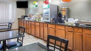 Una cocina de hotel con barra de desayuno buffet, que incluye un refrigerador, máquina para hacer gofres y diversos alimentos.