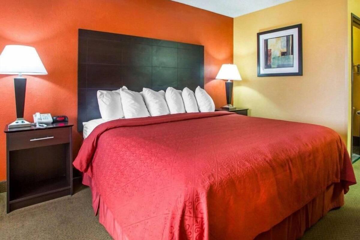 A hotel room with a large bed, two bedside tables with lamps, a framed picture on the wall, and a door to the right.