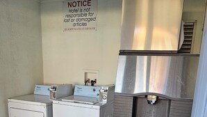 A laundry room with industrial washers and dryers, a notice on the wall, and a doormat. - Travel Inn & Suite (Springerville)