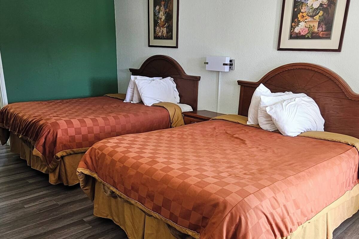 A hotel room with two beds, wooden flooring, a green accent wall, and a framed floral painting.