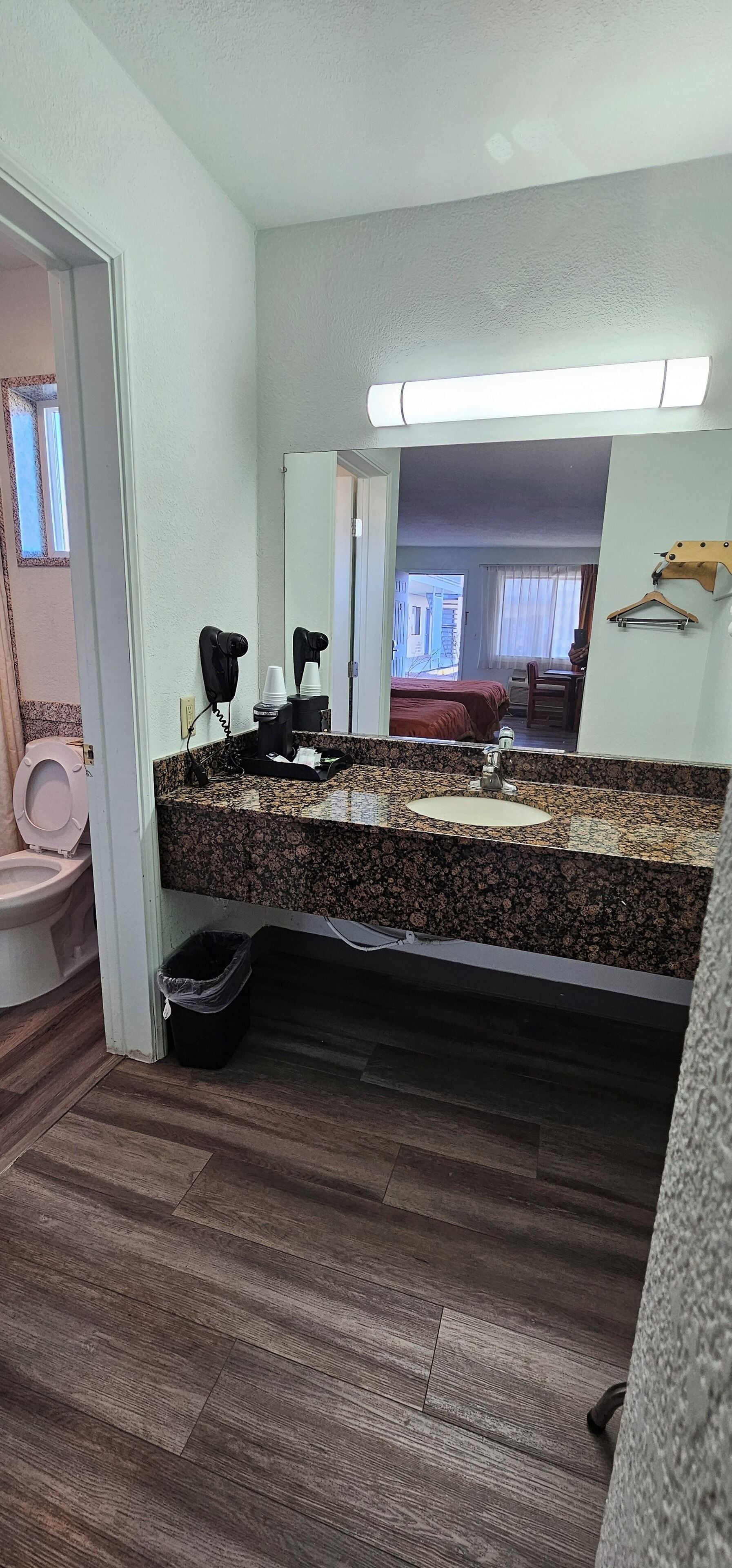 Ein Badezimmer mit einer Granit-Arbeitsplatte, einem Waschbecken, einem Spiegel, einem Föhn und einem Mülleimer.