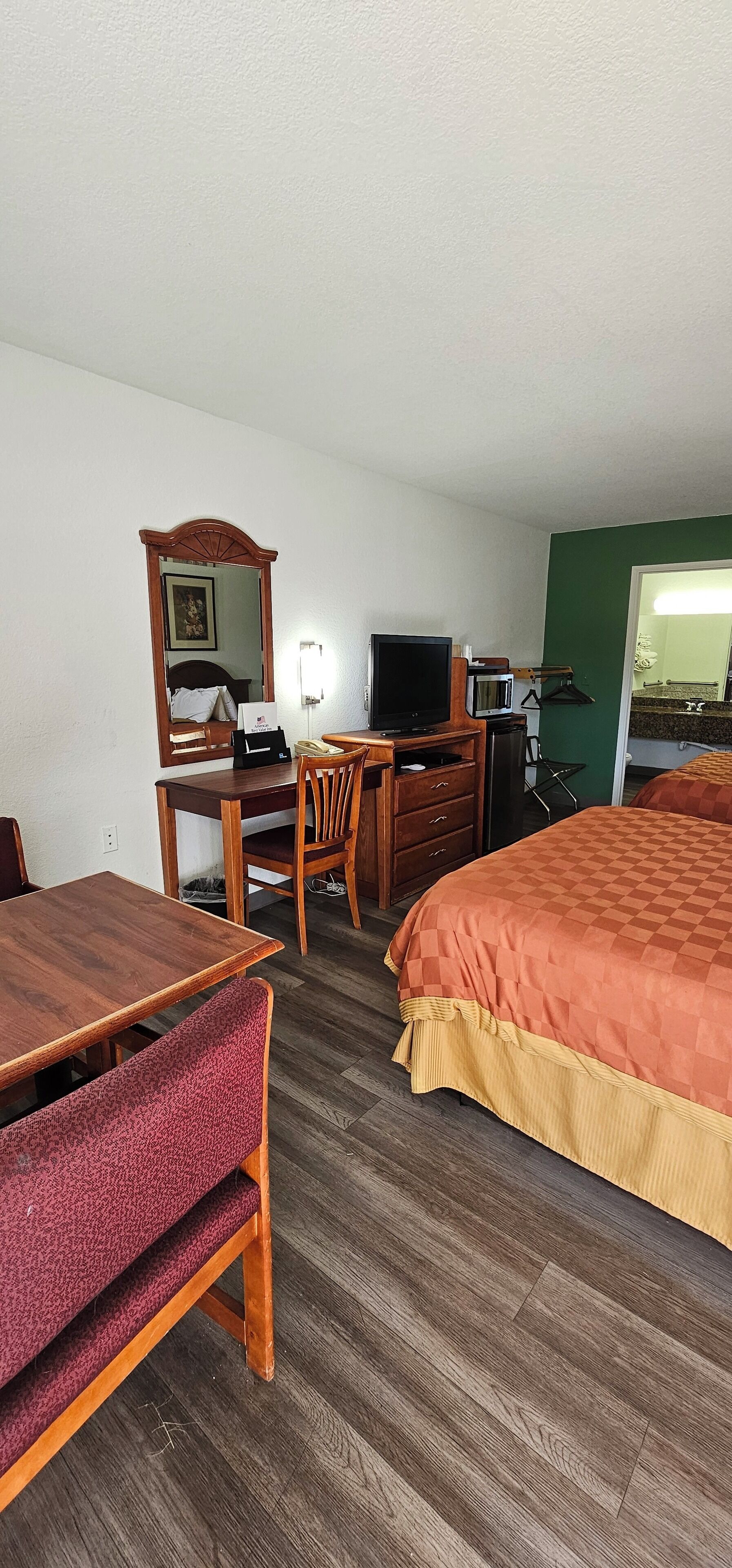 Een hotelkamer met een houten bureau, een televisie, een magnetron, een bed met oranje dekbedovertrek en een groene wand.