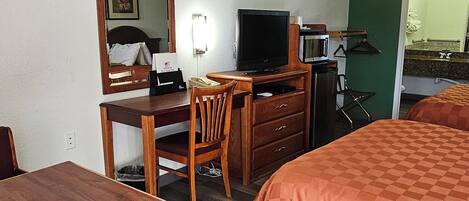 Een hotelkamer met een houten bureau, een televisie, een magnetron, een bed met oranje dekbedovertrek en een groene wand.