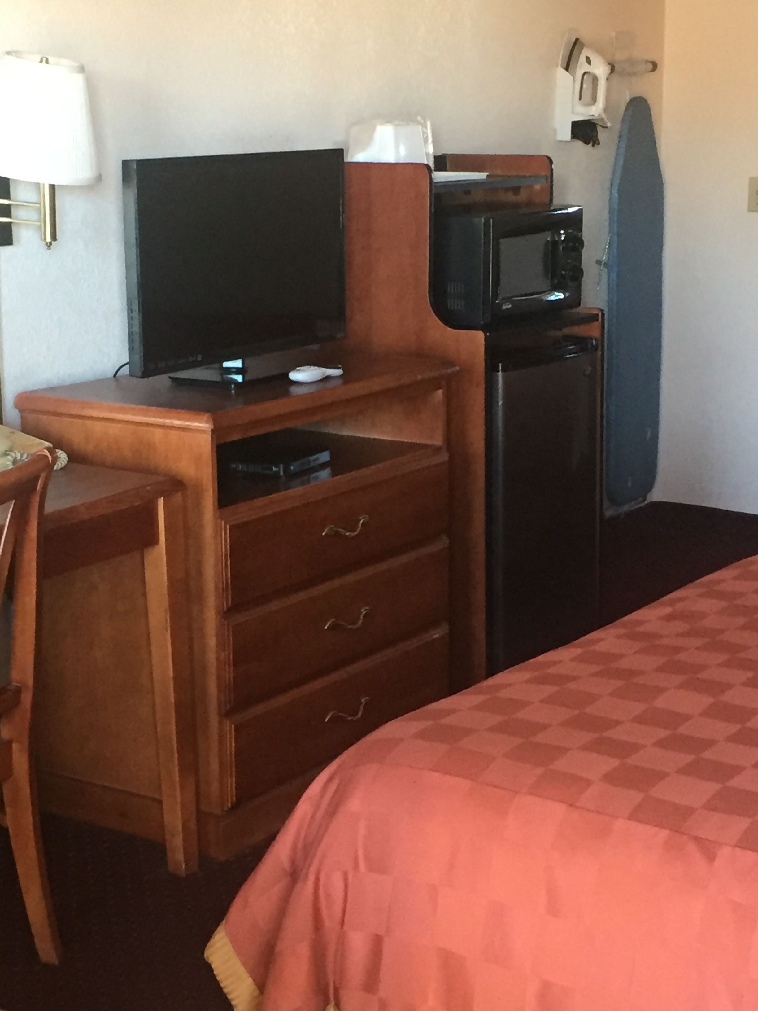 A hotel room with a wooden desk, a television, a microwave, a coffee machine, and a bed with a checkered bedspread.