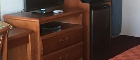 Habitación de hotel con un escritorio de madera, televisión, microondas, cafetera y cama con colcha a cuadros.