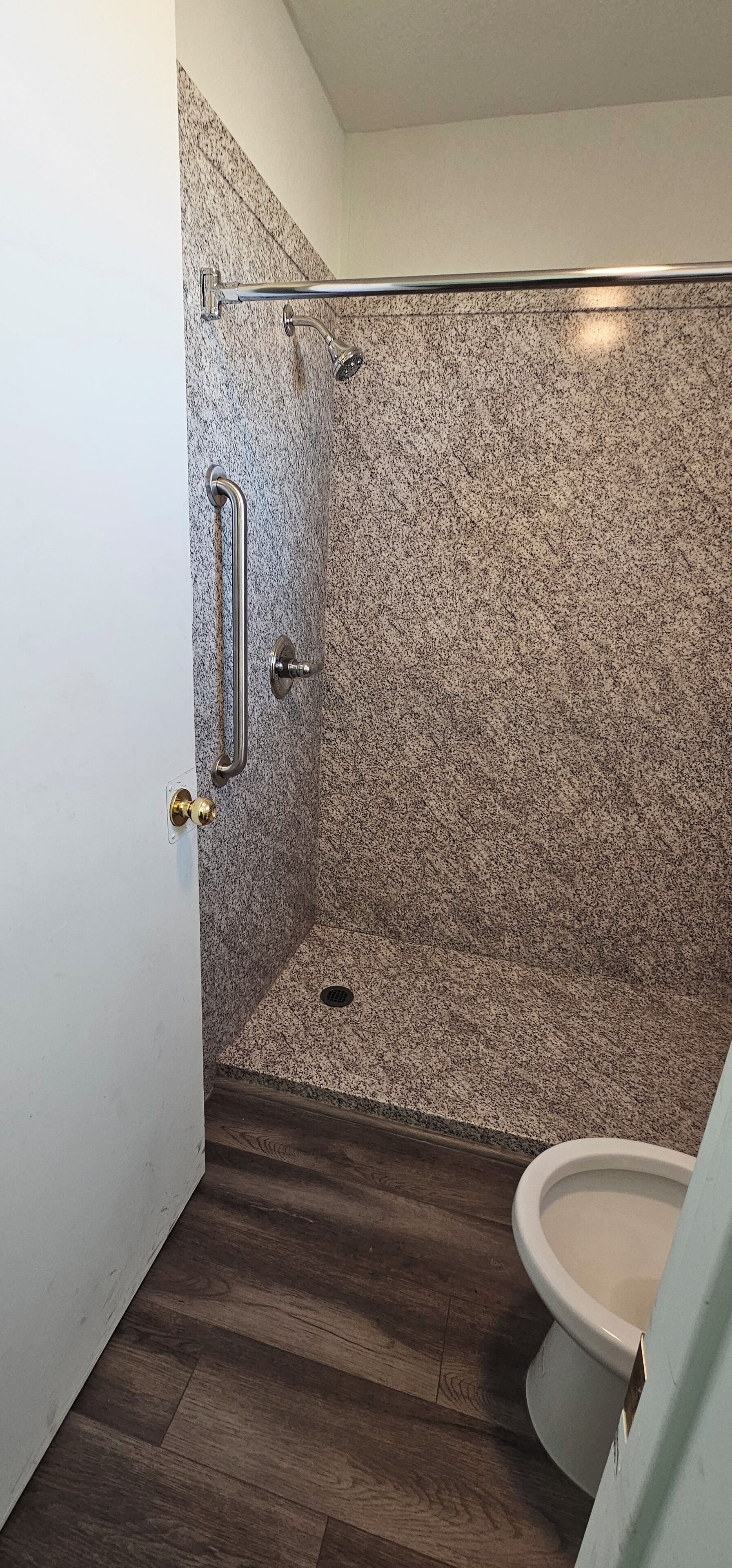 Ein Badezimmer mit Dusche, Toilette und einer Tür mit Griff.