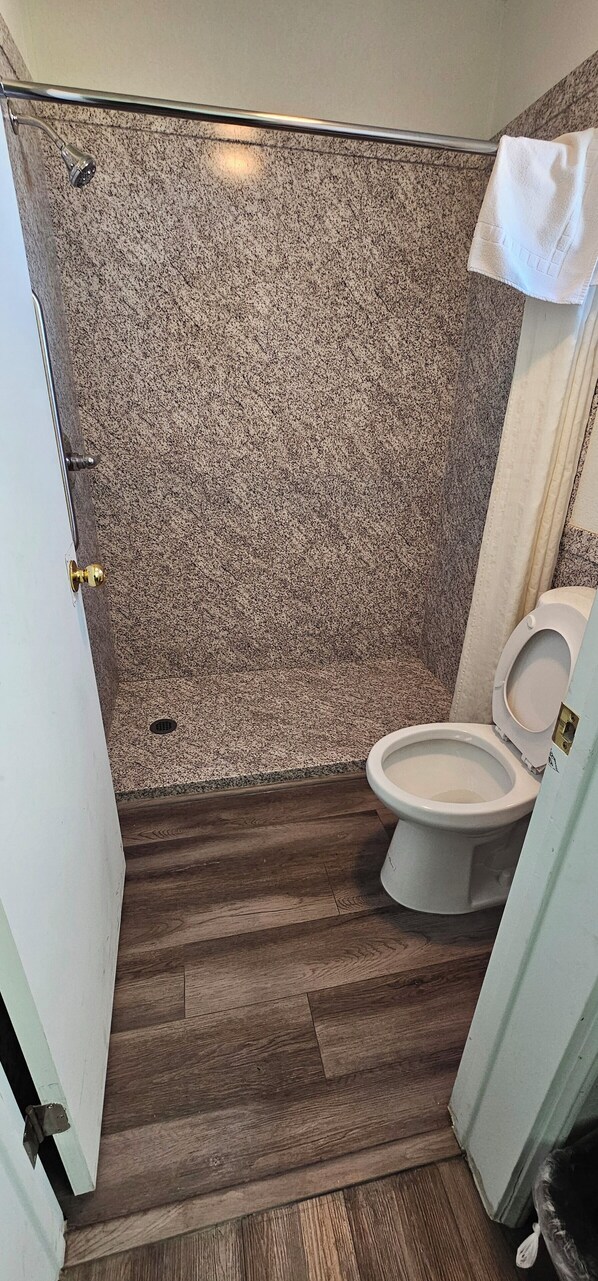 A bathroom with a shower, a toilet, and a wooden floor. - Travel Inn & Suite (Springerville)