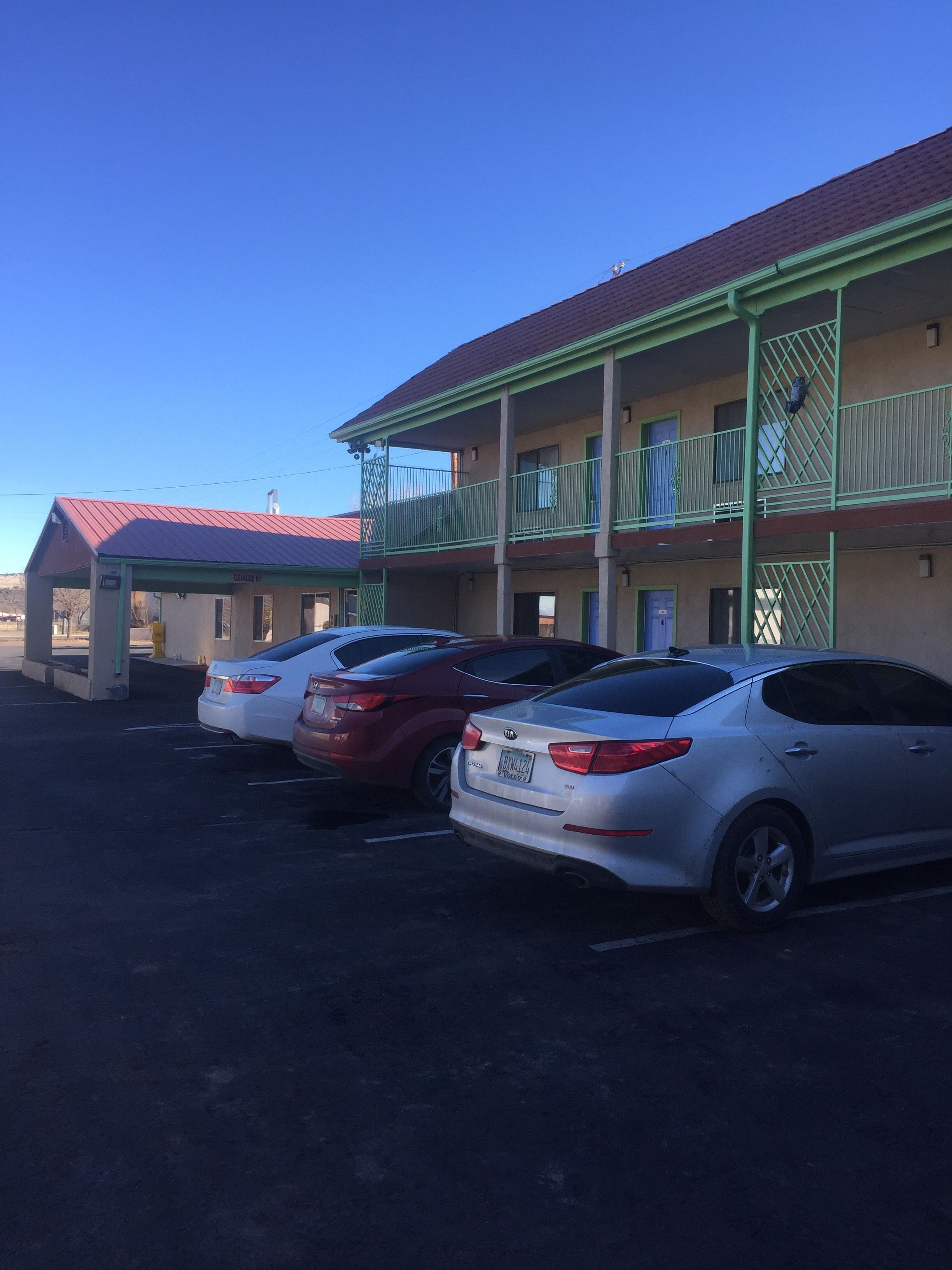 A motel with a red roof and green balconies. There are three cars parked in front.