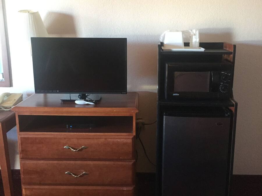 A hotel room with a wooden desk, a flat-screen TV, a small refrigerator, and a microwave.