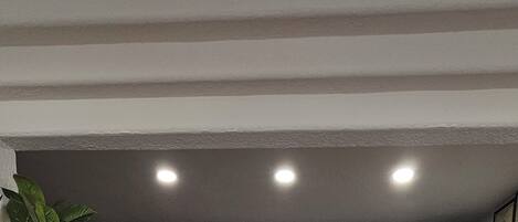 A room with a dark green wall, a ceiling with recessed lighting, and a shelf with framed pictures.