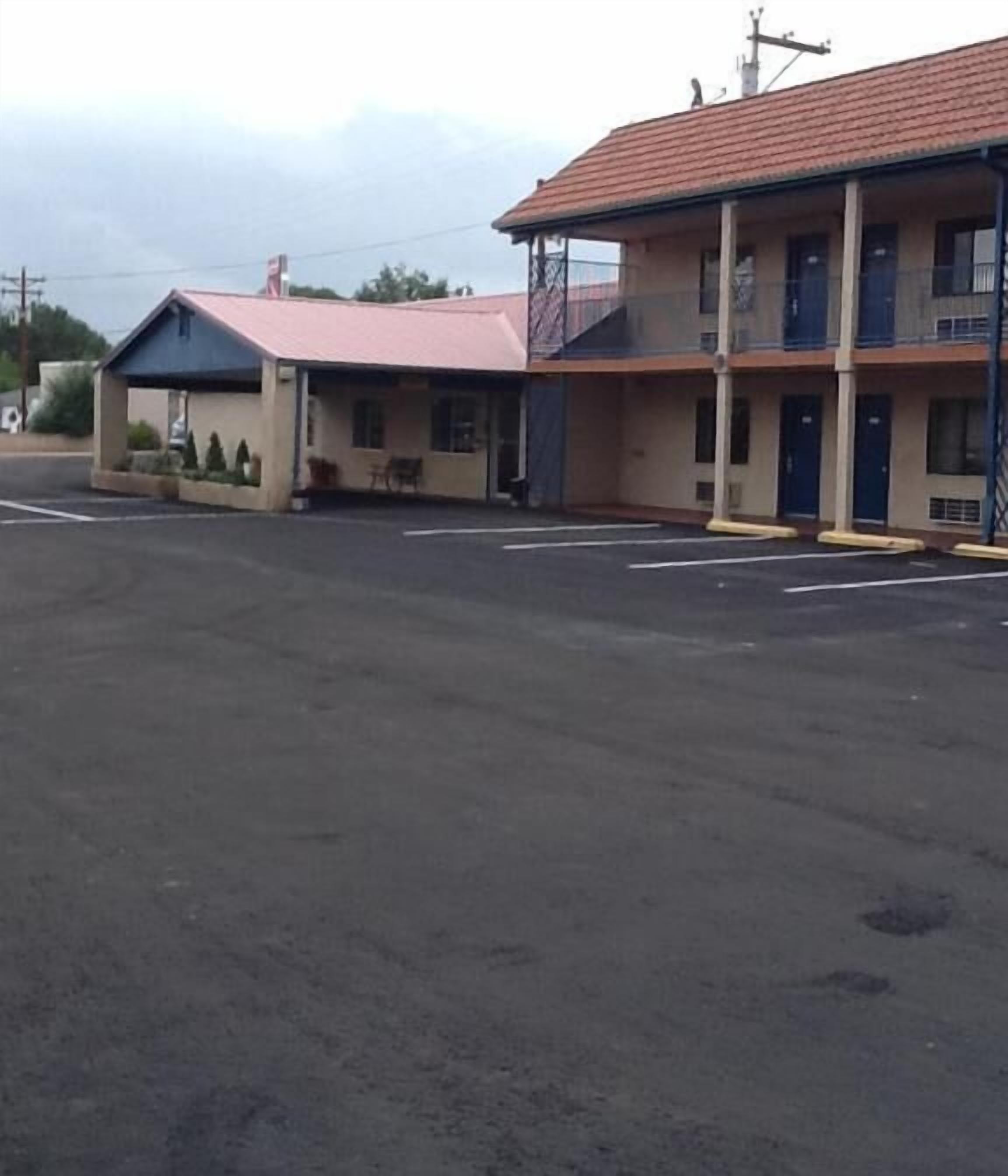 Un motel con una estructura de dos pisos, una zona de estacionamiento techada y un pequeño espacio al aire libre para sentarse.