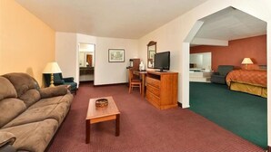 A hotel room with a sofa, a desk with a computer, a TV, a bed, and a small table. - Travel Inn & Suite (Springerville)