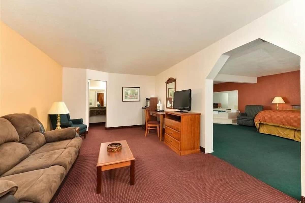 A hotel room with a sofa, a desk with a computer, a TV, a bed, and a small table.