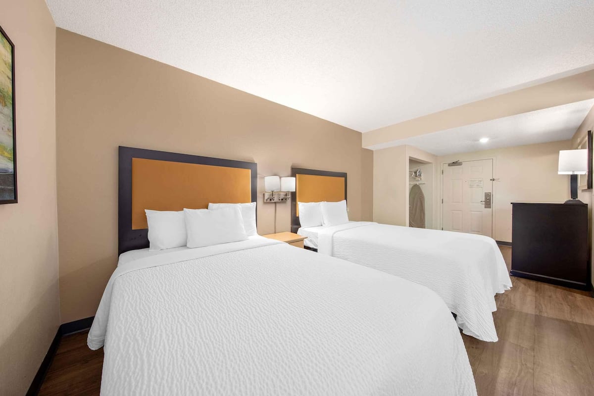 A hotel room with two beds, a desk, a lamp, and a door leading to a bathroom.