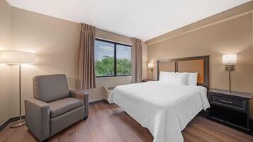 A hotel room with a bed, a chair, a nightstand, a lamp, and a window with curtains.