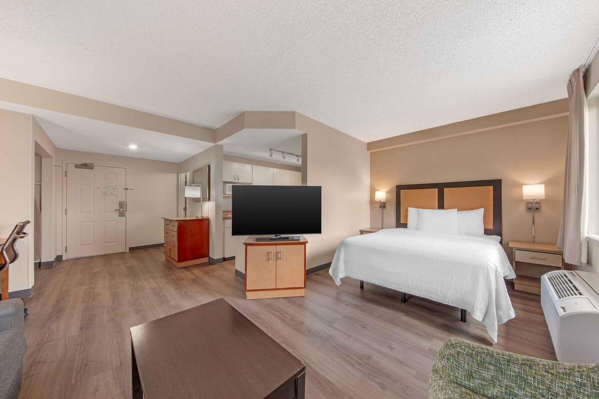 A hotel room with a bed, TV, desk, and kitchenette.