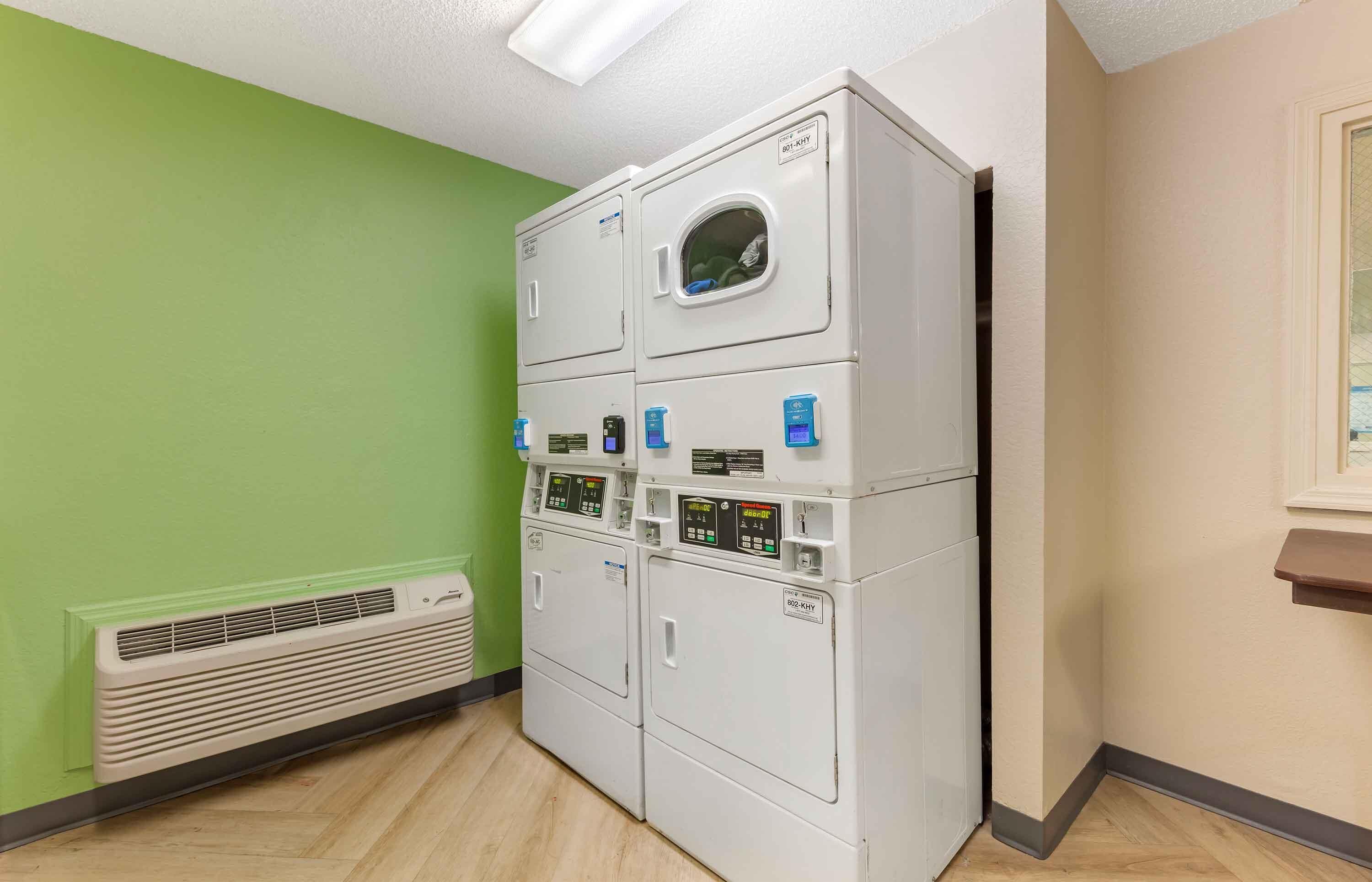 A laundry room with stacked washers and dryers, a vent, and a green wall.