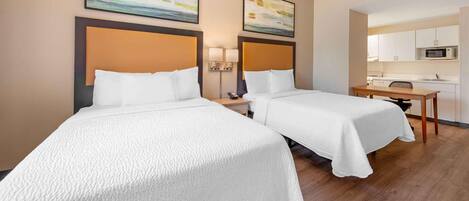 A hotel room with two beds, a desk, a chair, a microwave, and a small kitchen area.