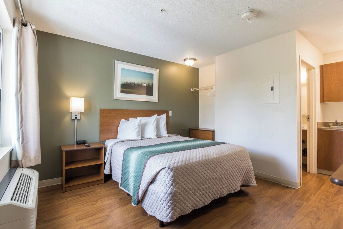 Une chambre d’hôtel bien rangée, avec un lit, des tables de chevet, une lampe et un tableau au mur.