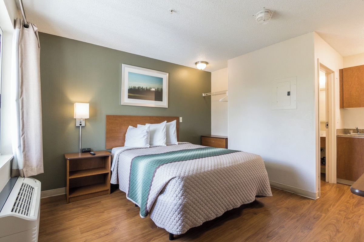 Una habitación de hotel con cama, mesita de noche, lámpara y un cuadro en la pared.