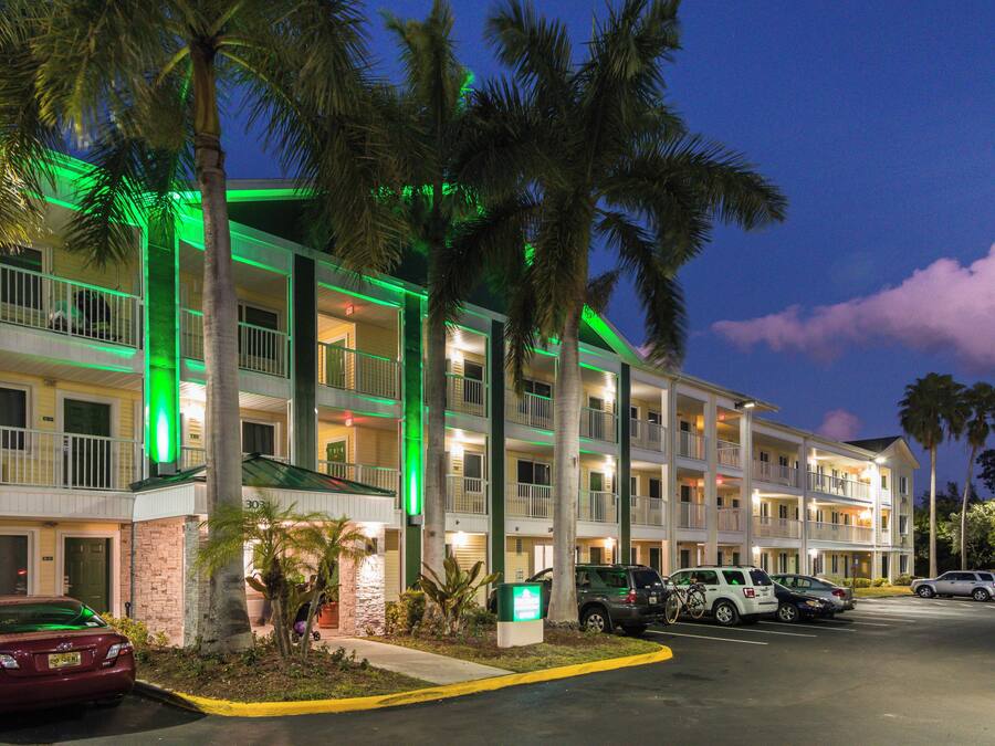 A multi-story hotel with a parking lot, palm trees, and a green-lit exterior.
