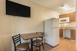 Una cocina compacta con una mesa de comedor, sillas, un refrigerador, un microondas y un televisor de pantalla plana montado en la pared.