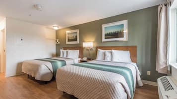 Habitación de hotel con dos camas, una mesita de noche con lámpara, un calentador en la pared y una puerta que da a otra habitación.