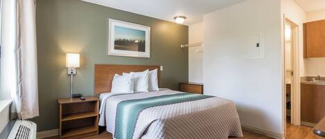 Una habitación de hotel con cama, mesitas de noche, lámpara, un cuadro en la pared y puerta al baño.