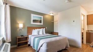 Una habitación de hotel con cama, mesitas de noche, lámpara, un cuadro en la pared y puerta al baño.