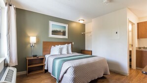 Ein Hotelzimmer mit Bett, Nachttischen, einer Lampe, einem Bild an der Wand und einer Tür zu einem Badezimmer.