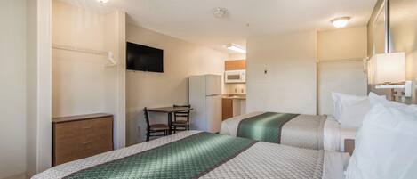 A hotel room with two beds, a desk, a chair, a television, and a kitchenette.