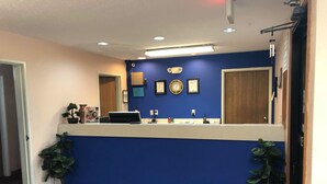 Zona de recepción con pared azul, mostrador de recepción, reloj, certificados enmarcados y plantas en macetas.