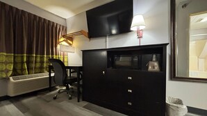 Habitación de hotel con televisor de pantalla plana, escritorio con silla, lámpara, calentador y cesto de basura.