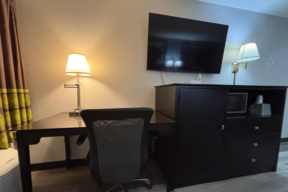 Una habitación de hotel con escritorio, silla, televisor y cómoda.