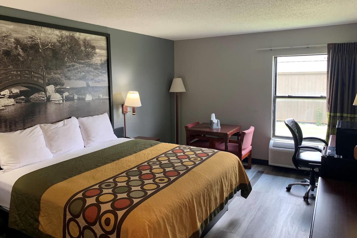 Una habitación de hotel con cama, escritorio, silla, lámpara y ventana.