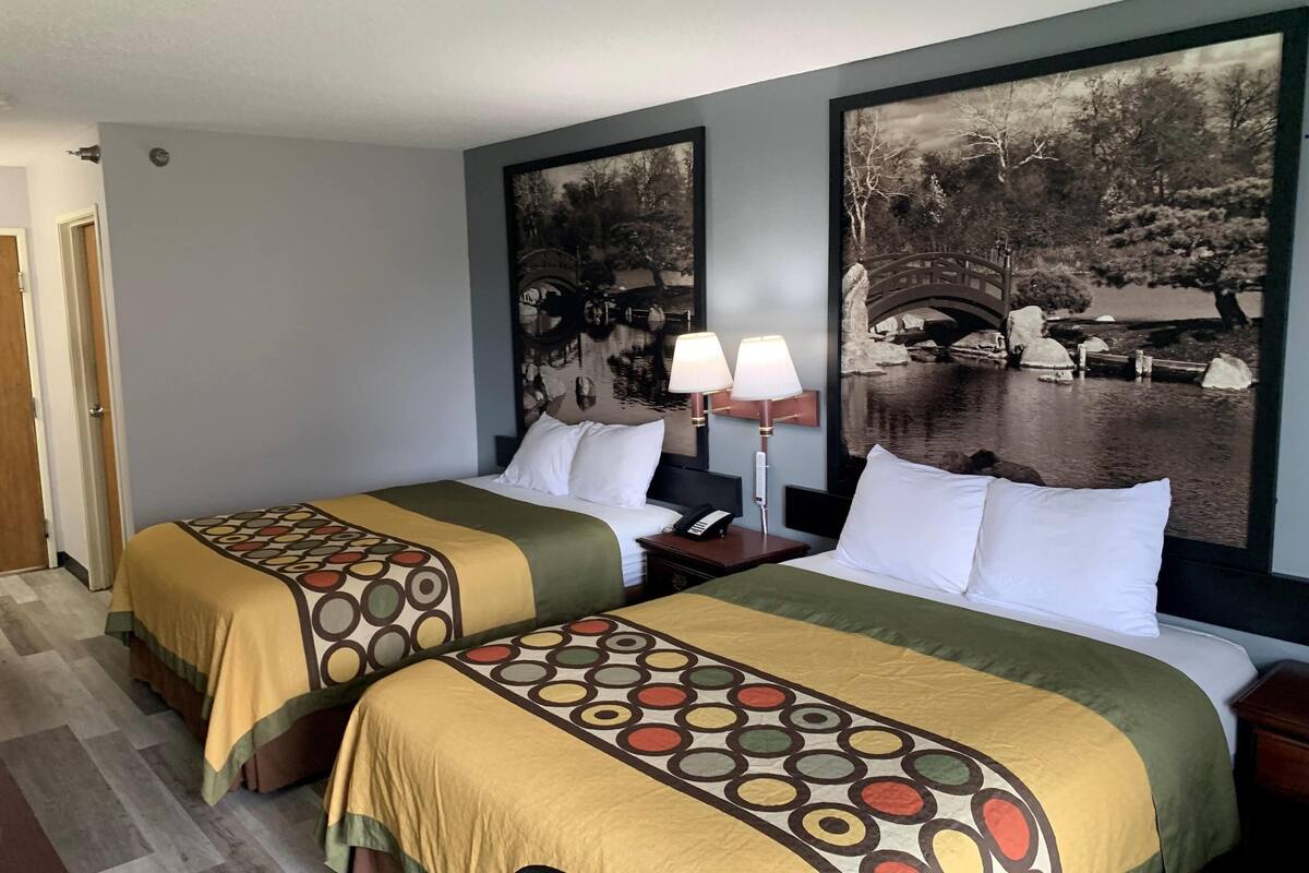 Habitación de hotel con dos camas, una mesita de noche con lámpara y dos cuadros grandes colgados en la pared.