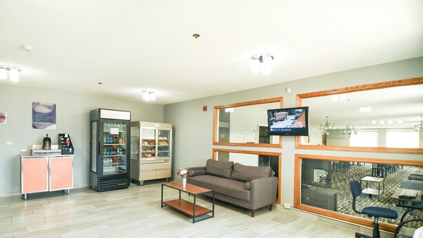 Un área de recepción con sofá, máquina de café, refrigerador y un televisor montado en la pared.