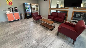 Un vestíbulo de hotel con sofás de cuero rojo, una estación de café, un refrigerador y un televisor montado en la pared.