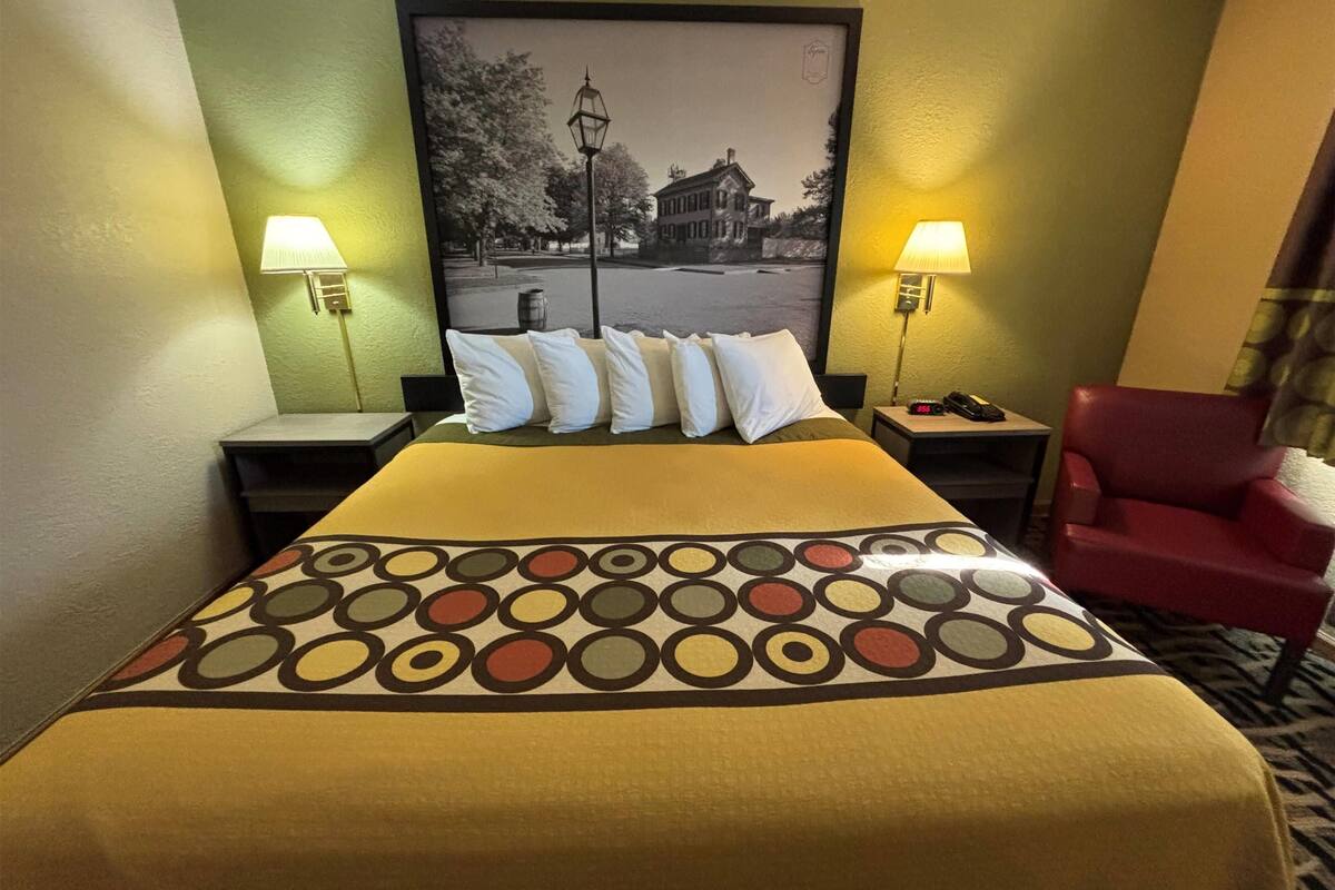 Ein Hotelzimmer mit einem Bett, zwei Nachttischlampen, einem roten Sessel und einem gerahmten Bild an der Wand.