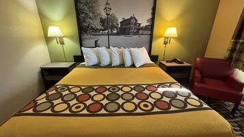 Una camera d'albergo con un letto, due lampade ai comodini, una sedia rossa e un quadro appeso al muro.