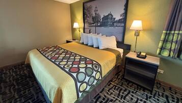 A hotel room with a bed, two bedside tables with lamps, a patterned carpet, and a large framed picture on the wall.