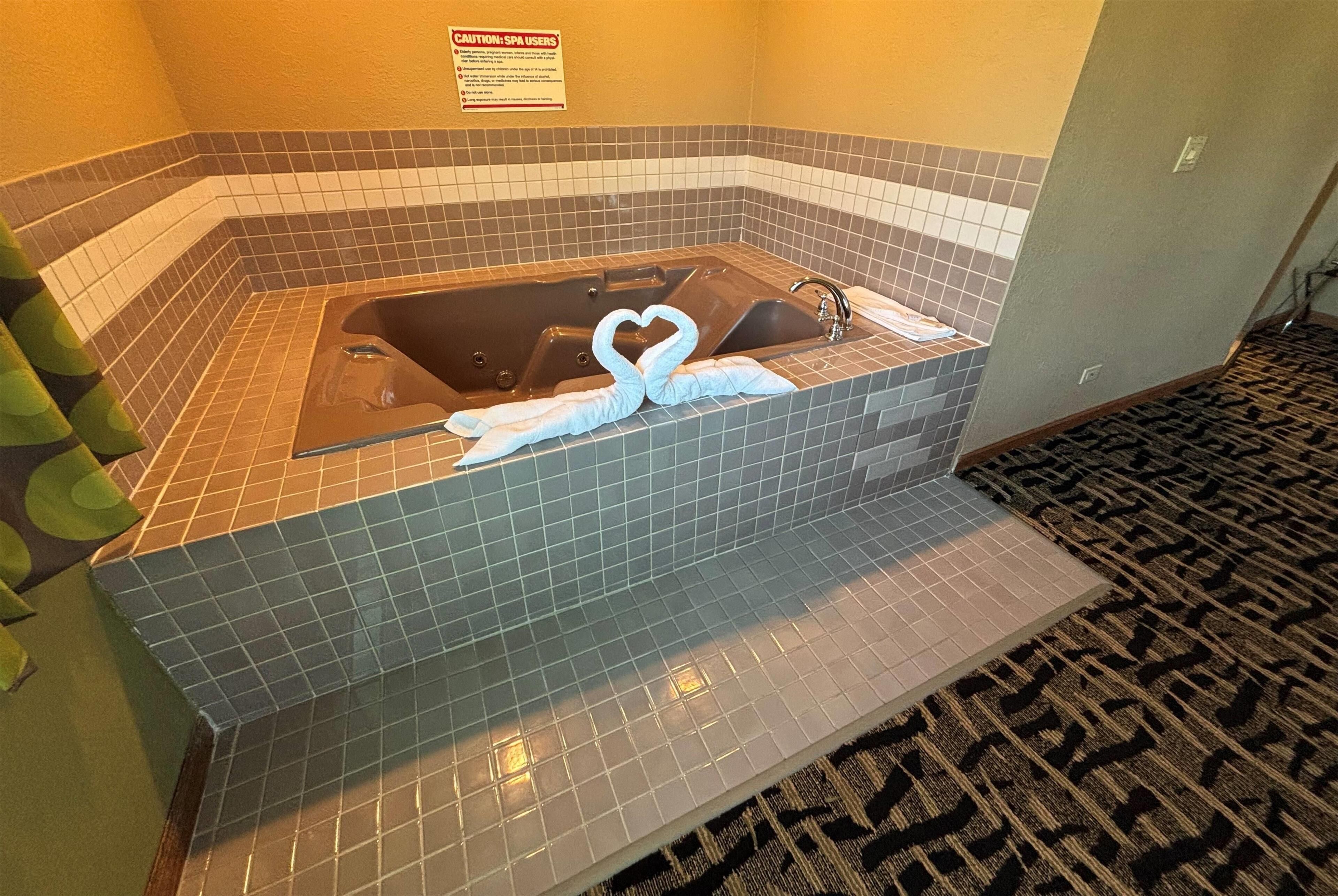 Zona de spa con bañera de azulejos, un cartel de precaución y una alfombra estampada.